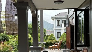 Un espacio al aire libre techado con una mesa y sillas de madera, plantas en macetas y una vista de una casa al fondo.