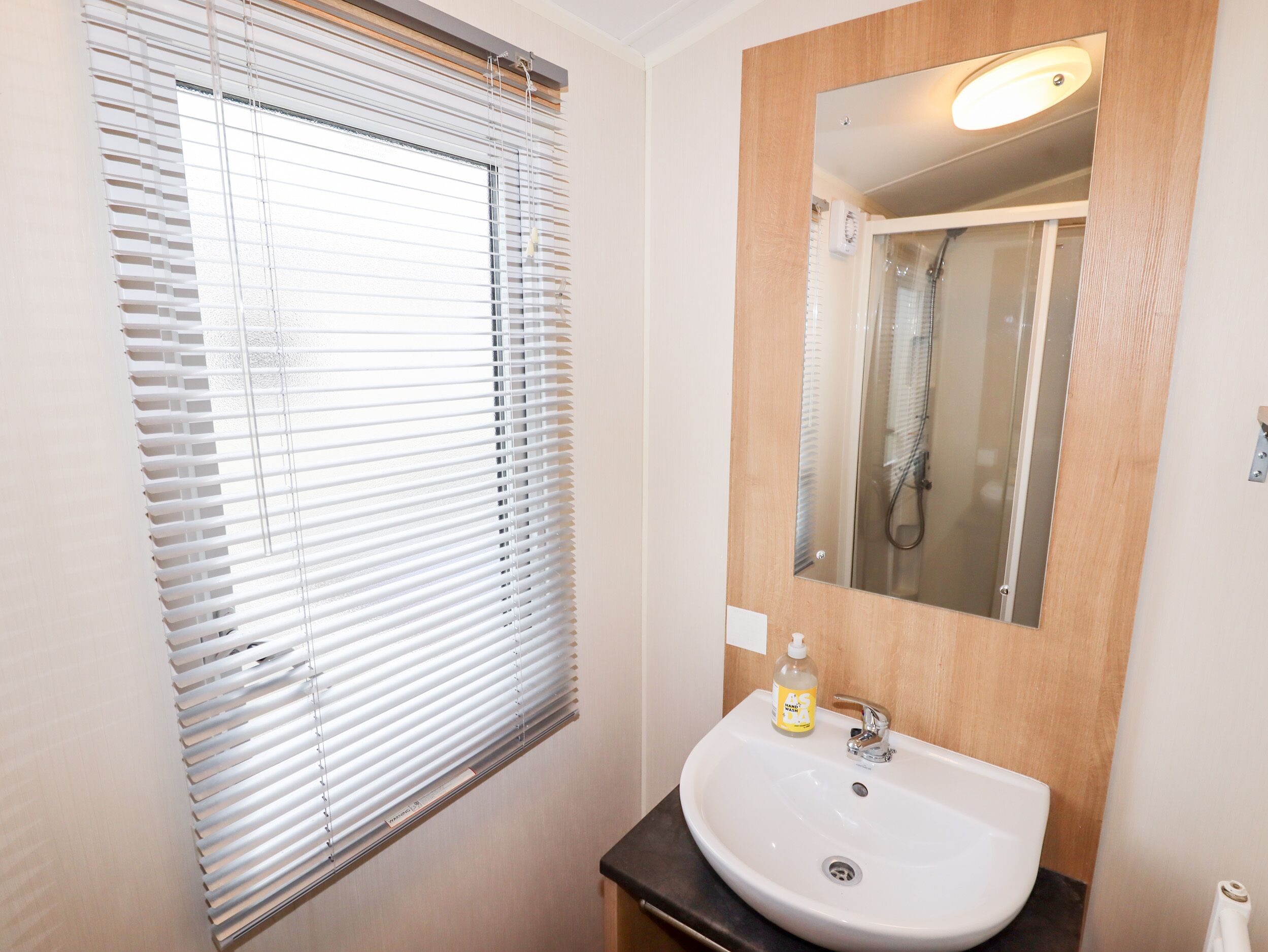 A bathroom with a white sink, a mirror, and a window with blinds.