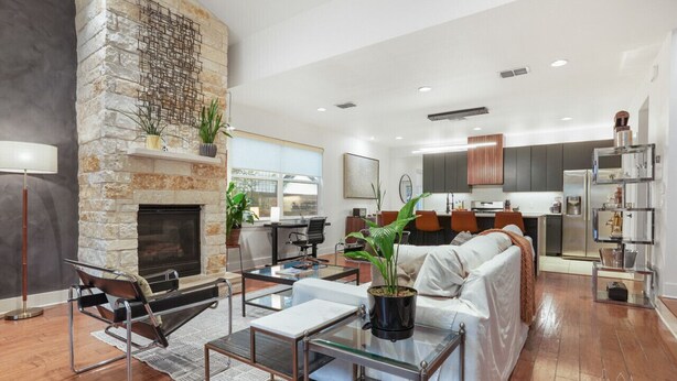 Una sala de estar moderna con chimenea de piedra, un sofá, una mesa de centro y una cocina al fondo.