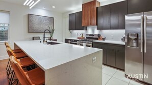 Una cocina moderna con una isla grande, armarios oscuros, electrodomésticos de acero inoxidable e iluminación colgante.