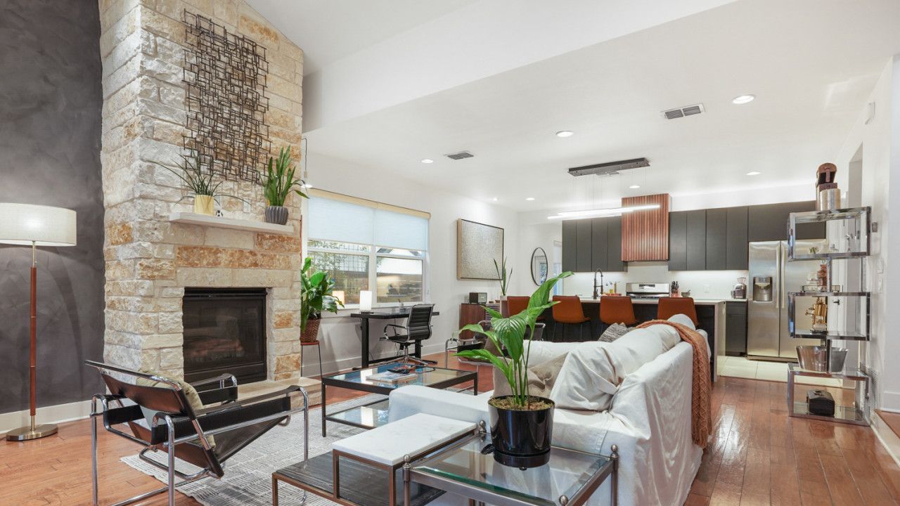 Un salon moderne avec une cheminée en pierre, un canapé, une table basse et une cuisine en arrière-plan.