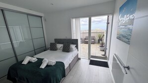 A bedroom with a bed, a sliding glass door to a balcony, and a view of the city. - 10 Quay Court (Newquay)