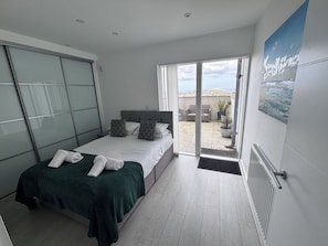 Une chambre avec un lit, une porte-fenêtre coulissante donnant sur un balcon et une vue sur la ville.
