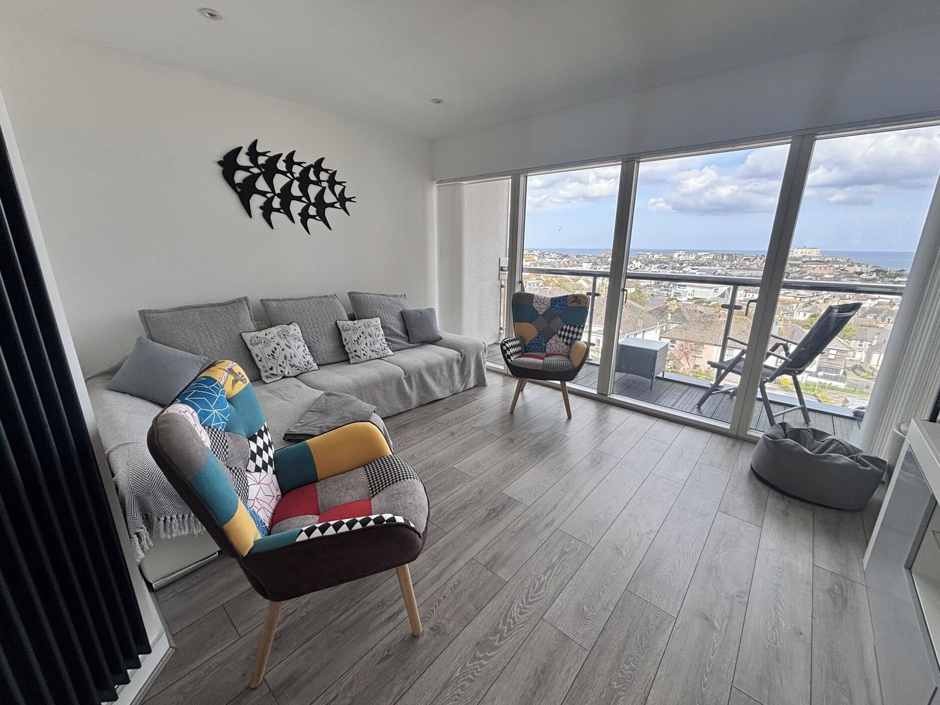 A modern living room with a grey sofa, colorful armchair, and a city view through large windows.