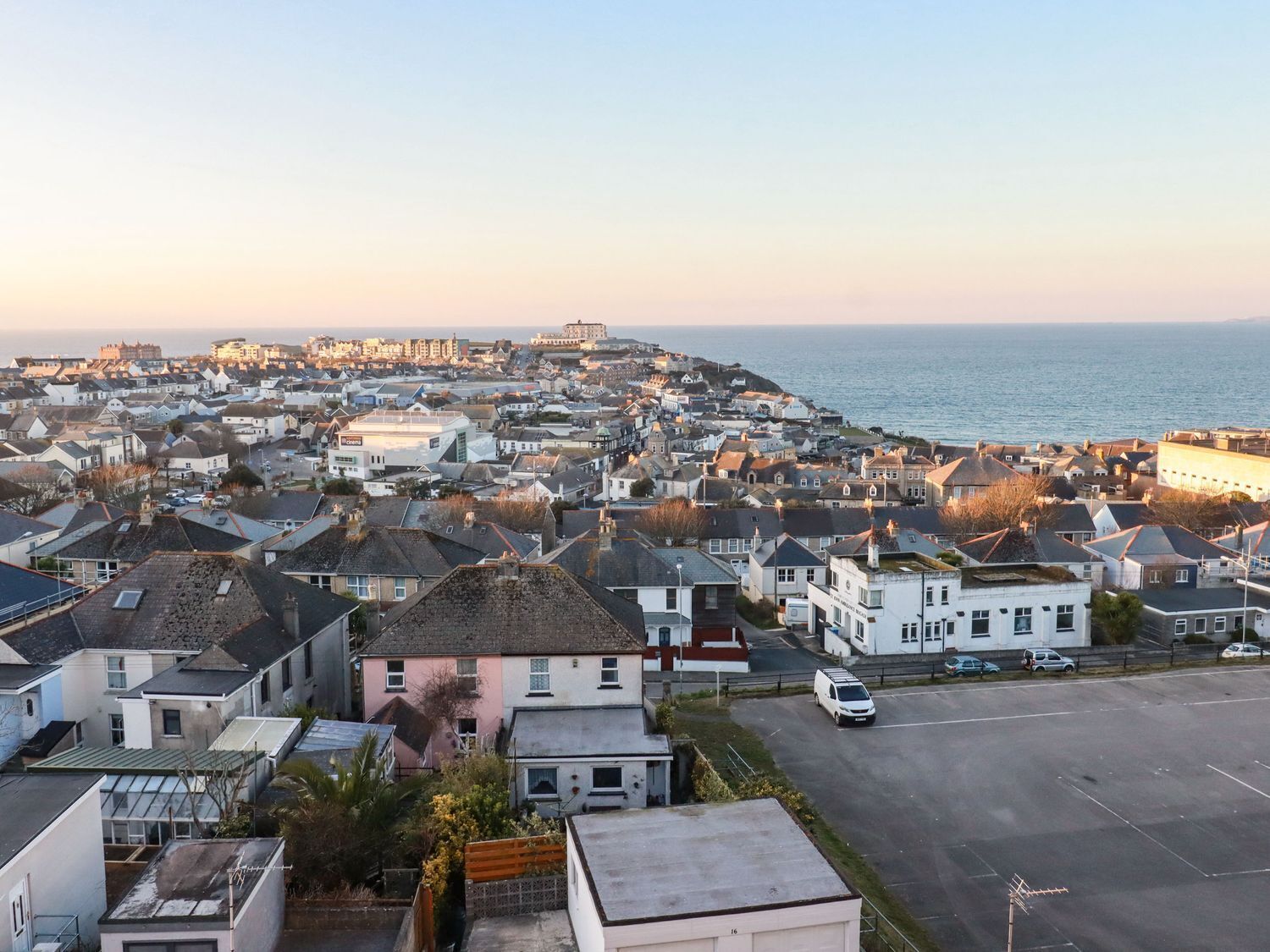 A coastal town with residential buildings, a parking area, and a view of the sea.