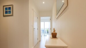 A hallway with a white door, a framed picture on the wall, and a potted plant on a white table. - 10 Quay Court (Newquay)