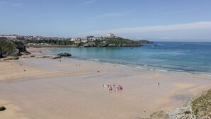 A beach with a large building on a hill, clear skies, and calm waters. - 10 Quay Court (Newquay)