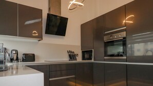 A modern kitchen with dark cabinets, a built-in oven, a microwave, and a coffee maker. - 10 Quay Court (Newquay)