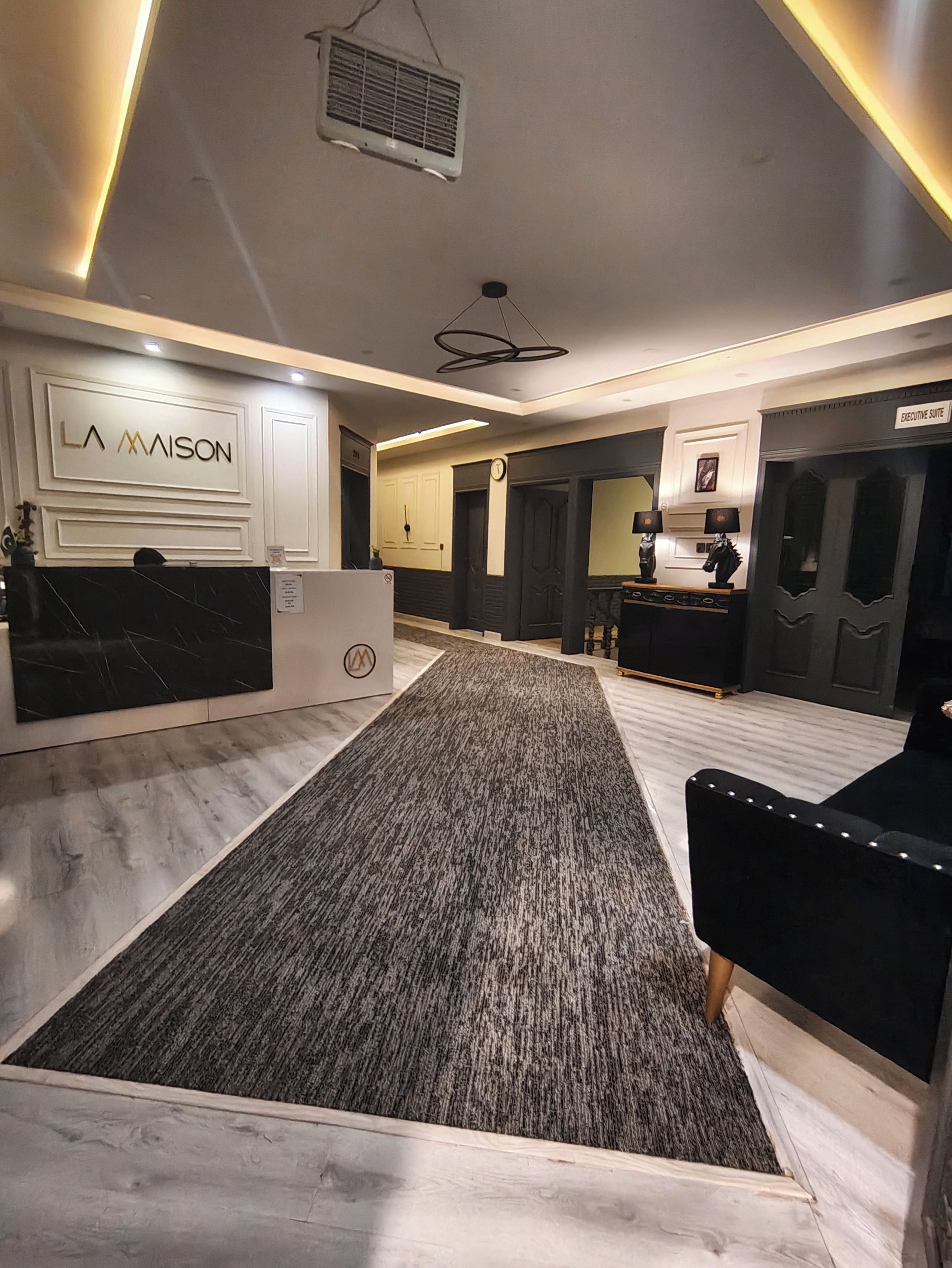 Un hall d’hôtel comprenant un comptoir d’accueil, un espace recouvert de moquette et un coin salon avec un canapé noir.
