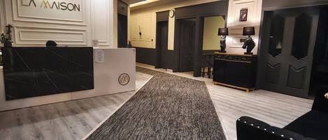 Un hall d’hôtel comprenant un comptoir d’accueil, un espace recouvert de moquette et un coin salon avec un canapé noir.