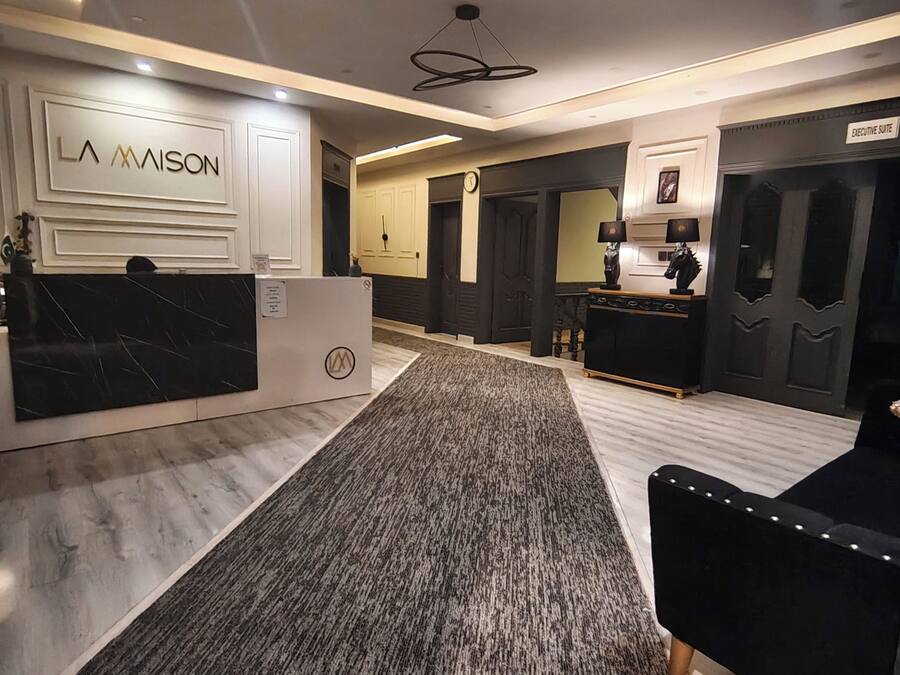 A hotel lobby with a reception desk, a carpeted area, and a seating area with a black sofa.