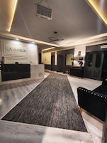 Un vestíbulo de hotel con una recepción, una zona alfombrada y un área de descanso con un sofá negro.