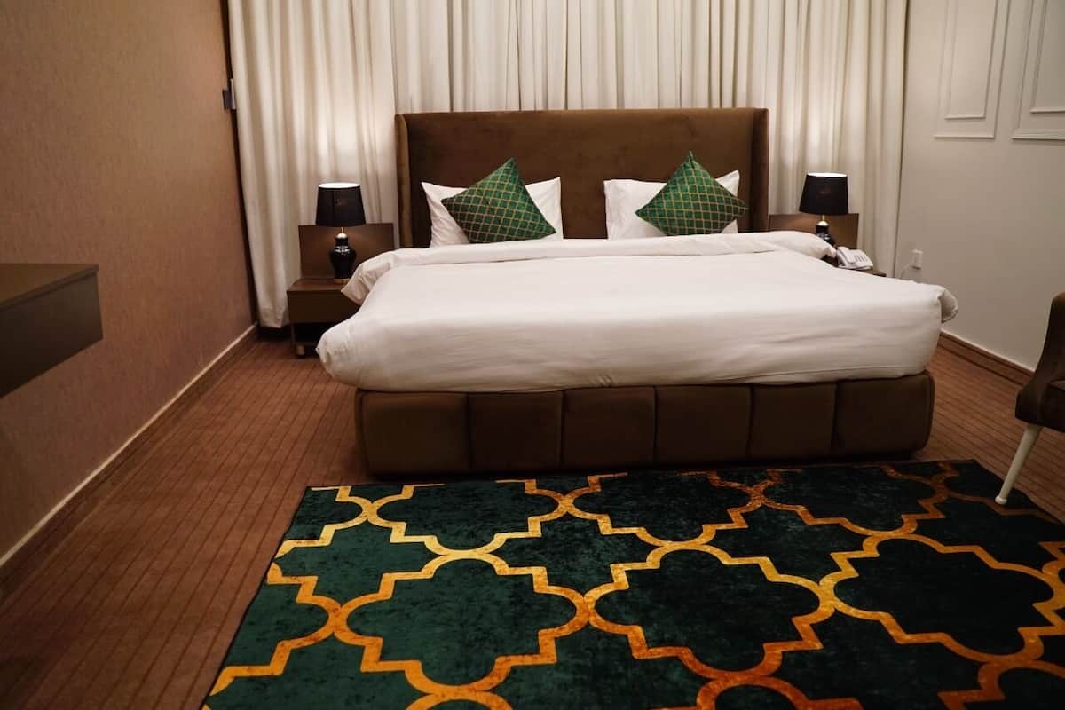 A hotel room with a large bed, two bedside tables with lamps, a patterned rug, and a window with curtains.