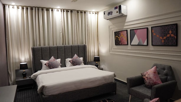 Ein Hotelzimmer mit einem großen Bett, zwei Nachttischen mit Lampen, einem grauen Sessel und einer Wand mit drei gerahmten Kunstwerken.