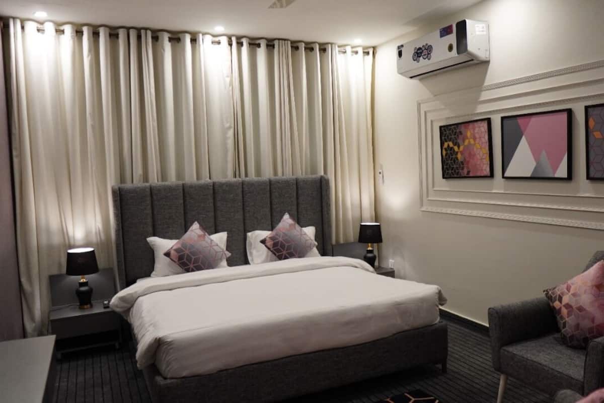 A hotel room with a large bed, two bedside tables with lamps, a grey armchair, and a wall with three framed artworks.