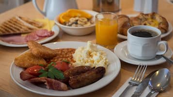 A breakfast table with plates of toast, beans, sausages, scrambled eggs, and a cup of coffee.