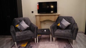Ein modernes Wohnzimmer mit zwei grauen Sesseln, einem kleinen schwarzen Couchtisch und einem an einer Holzkommode befestigten Flachbildfernseher.