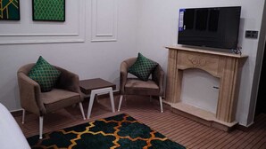 Ein Wohnzimmer mit zwei Sesseln, einem kleinen Tisch, einem Fernseher auf einem Schrank und einem Kamin.