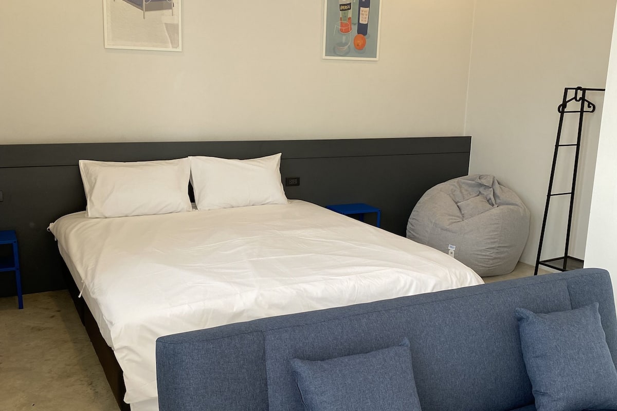 Un dormitorio moderno con una cama grande, un sofá gris y un sillón informal.