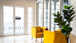 A bright room with large windows, a yellow sofa, and a potted plant. - PIER 808 Hostel (Bangkok)
