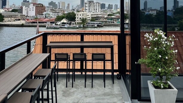 A rooftop terrace with a view of a city skyline, a wooden table with chairs, and a potted plant. - PIER 808 Hostel (Bangkok)