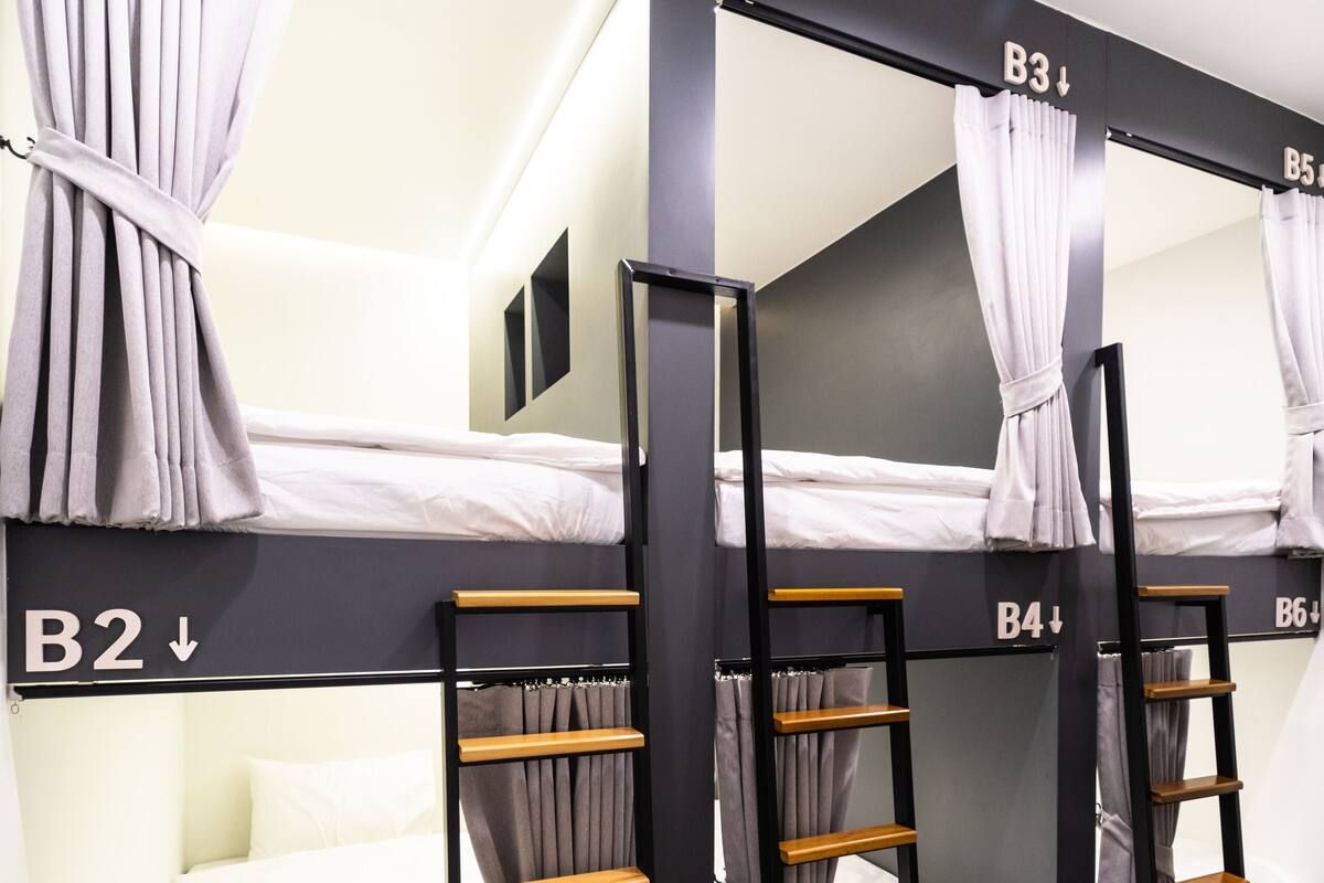 Dormitorio con literas de tres niveles, etiquetados B1, B2, B3 y B4. Cada litera tiene una cortina y una escalera de madera.