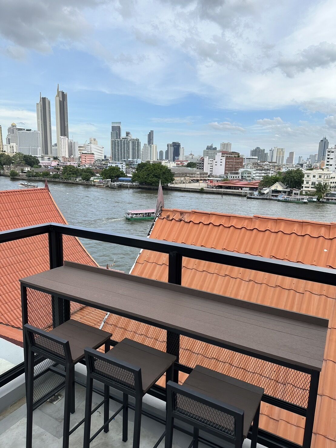 Ein Balkon mit Tisch und Stühlen mit Blick auf einen Fluss, auf dem Boote fahren, und eine Stadtlandschaft im Hintergrund.