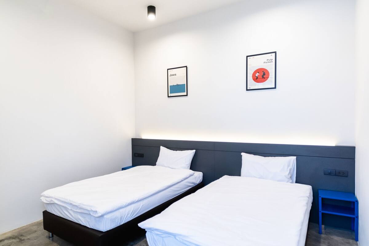 Una habitación de hotel moderna con dos camas individuales, suelo de concreto gris y dos cuadros en la pared.