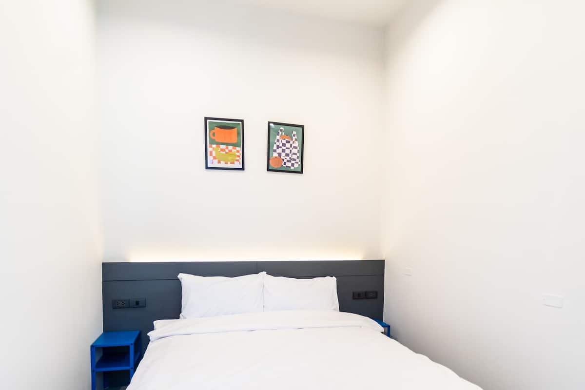 Una habitación de hotel moderna con una cama grande, una mesita de noche azul y dos cuadros en la pared.