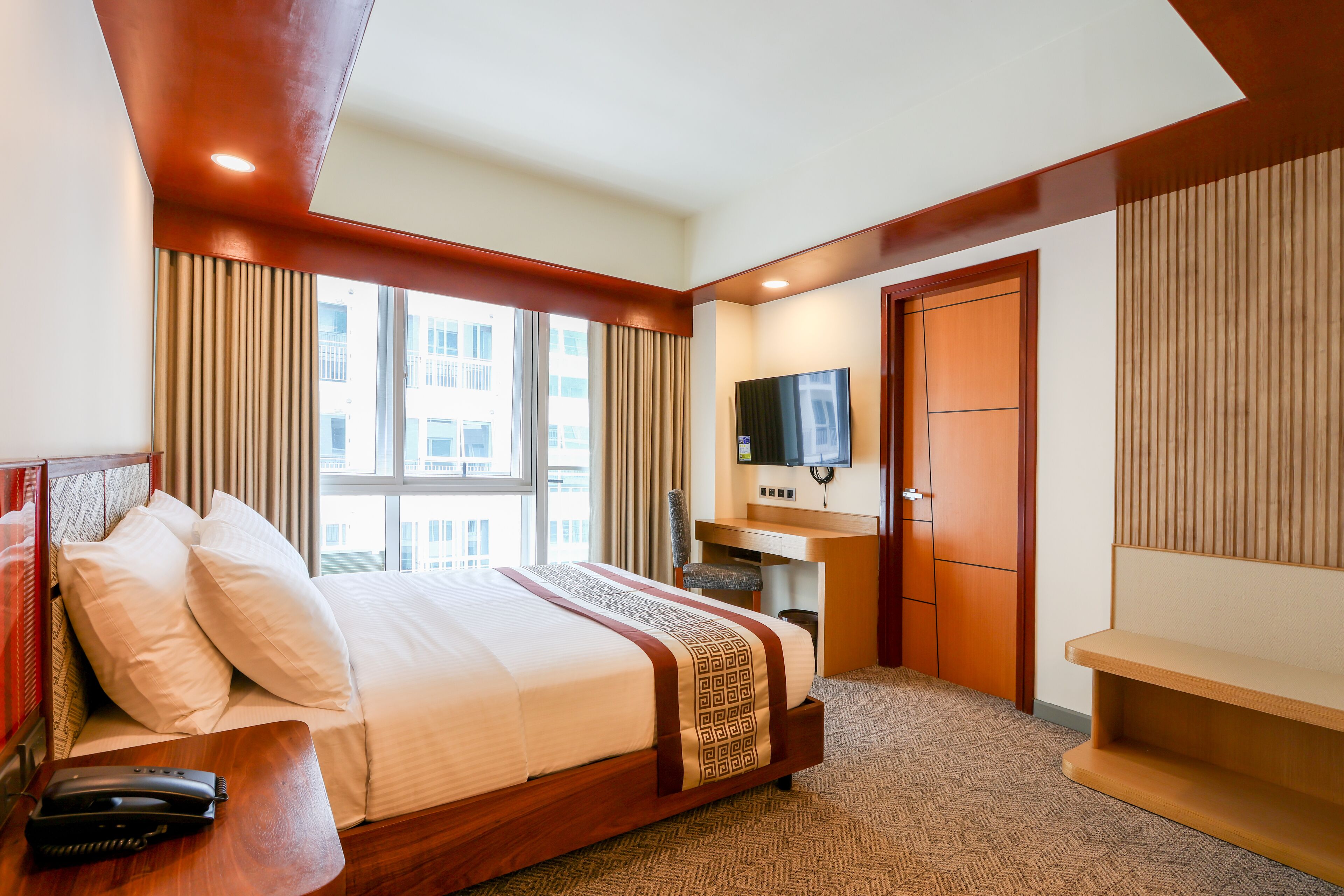 A hotel room with a large bed, a desk, a television, and a window with curtains.