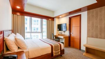 Ein Hotelzimmer mit einem großen Bett, einem Schreibtisch, einem Fernseher und einem Fenster mit Vorhängen.