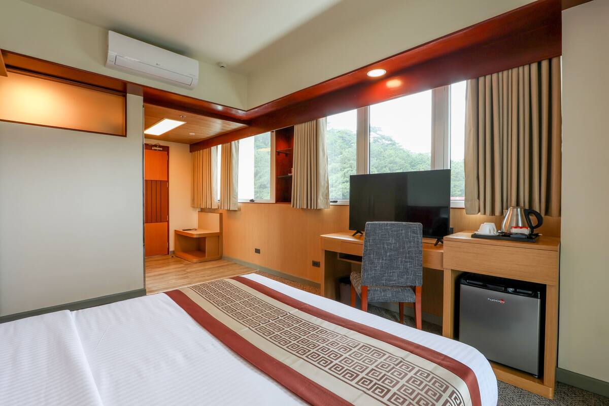 Habitación de hotel con cama, escritorio, silla, televisor y un refrigerador pequeño.