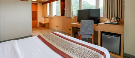 Habitación de hotel con cama, escritorio, silla, televisor y un refrigerador pequeño.