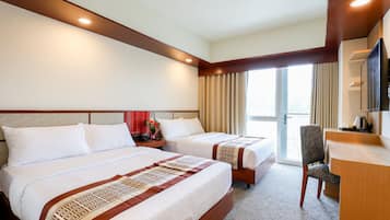 A hotel room with two beds, a desk, a chair, and a large window.