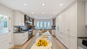 A modern kitchen with white cabinetry, a central island with a beige cloth and sunflowers, and a view of the outdoors through large windows.