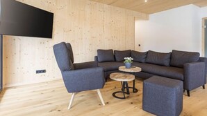 Un salon moderne avec un canapé d’angle, une petite table ronde et un téléviseur à écran plat fixé au mur.