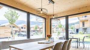 Un espace de restauration moderne avec une table et des chaises en bois, de grandes fenêtres offrant une vue sur les bâtiments et le paysage environnants.