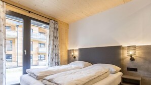 Une chambre à coucher avec un lit, deux tables de chevet avec des lampes, une fenêtre avec des rideaux et une vue sur un bâtiment à l’extérieur.