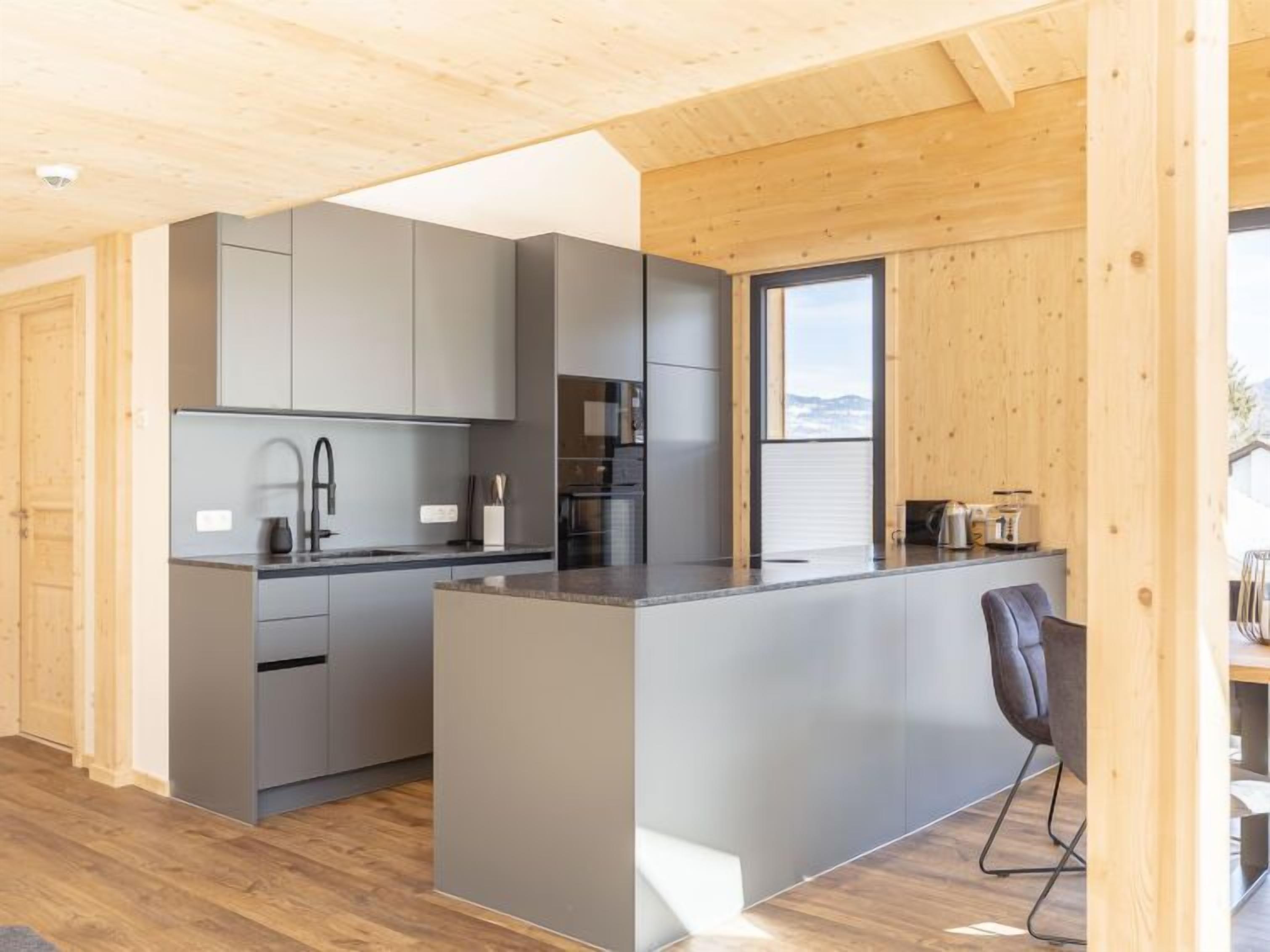 Une cuisine moderne avec des meubles gris, un îlot central et une chaise noire.