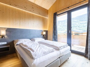 Un dormitorio con cama, mesitas de noche y un ventanal con vistas a un paisaje montañoso.