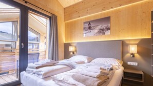 Une chambre moderne avec un grand lit, des murs en bois, une vue à travers une porte vitrée et un tableau représentant un paysage de montagne au-dessus du lit.