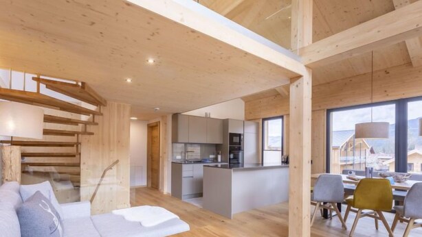 Un intérieur moderne avec un escalier en bois, un coin repas avec des chaises et une cuisine en arrière-plan.