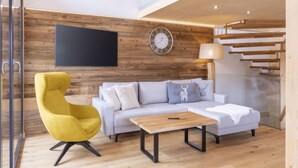 Un salon moderne avec un canapé, un fauteuil jaune, une table basse, une horloge et un escalier.