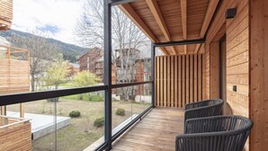 Une terrasse en bois dotée d’une balustrade en verre, offrant une vue sur un quartier résidentiel et les montagnes.