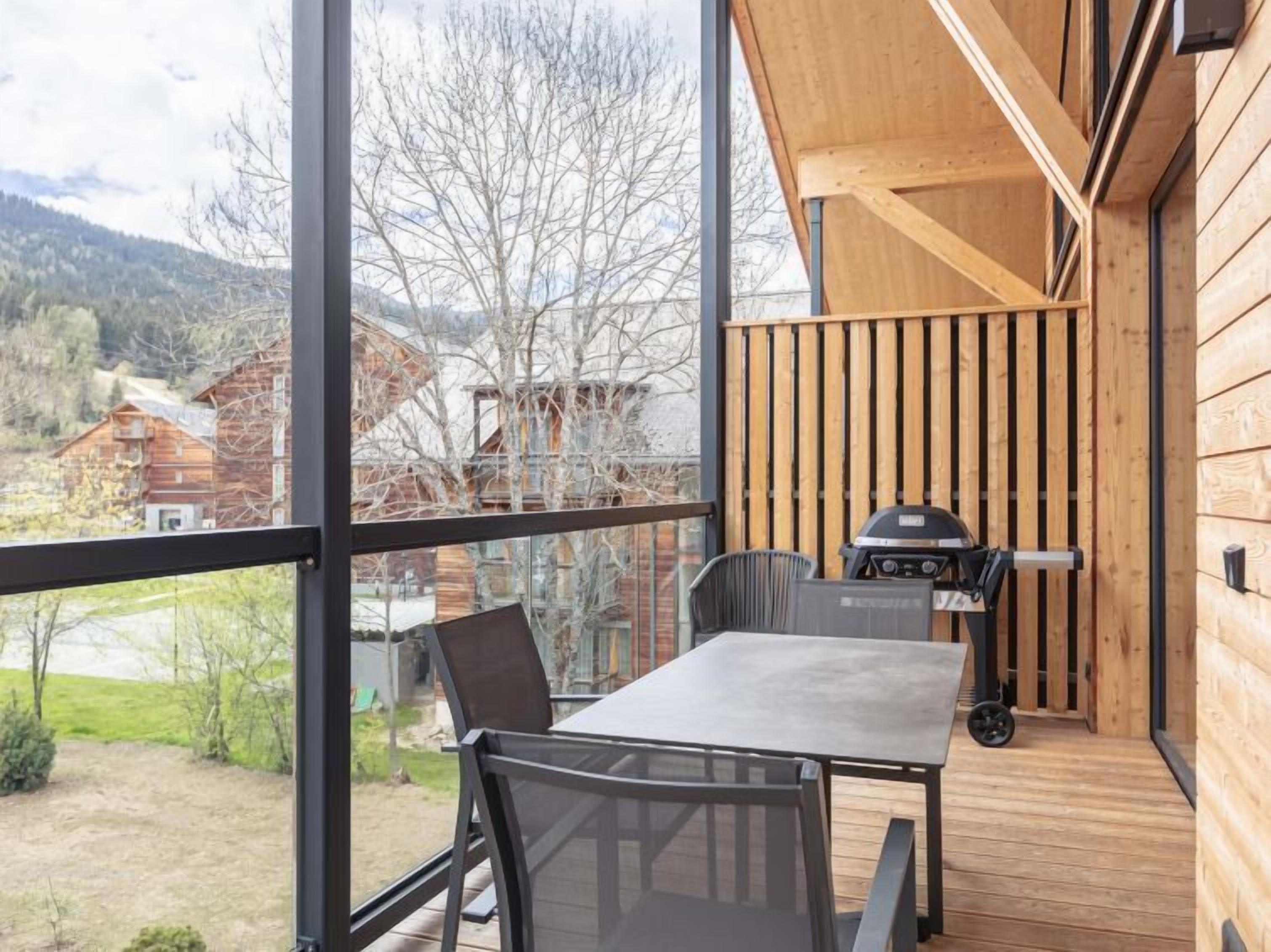 Ein Balkon mit Tisch, Stühlen, einem Grill und Blick auf Häuser und Bäume.