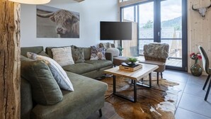 A modern living room with a green sofa, a wooden coffee table, and a large window offering a view of the outdoors. - Penthouse # 4b mit Sauna&Außenbadewanne by Interhome (Sankt Georgen am Kreischberg)