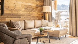 Una sala de estar moderna con un muro de madera, un sofá, una mesa de centro y vista a un paisaje nevado a través de un ventanal grande.