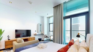 A modern hotel room with a large bed, a flat-screen TV, a desk, and a view of the city.