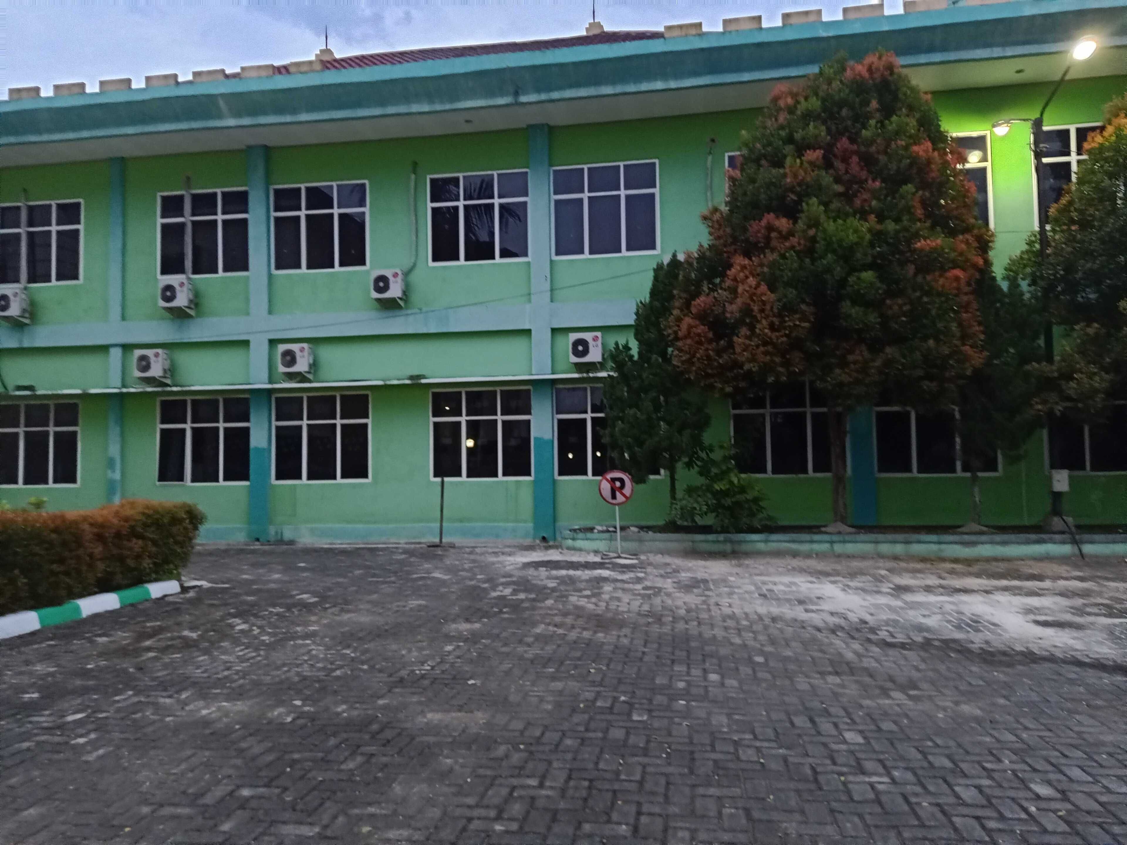 A green building with multiple windows and air conditioning units, a no parking sign, and a paved area with a hedge.