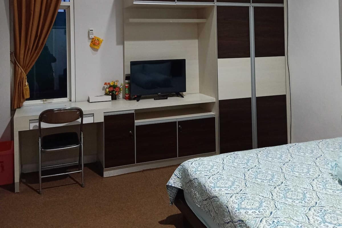 Un dormitorio con cama, escritorio con televisor, armario y ventana con cortinas.